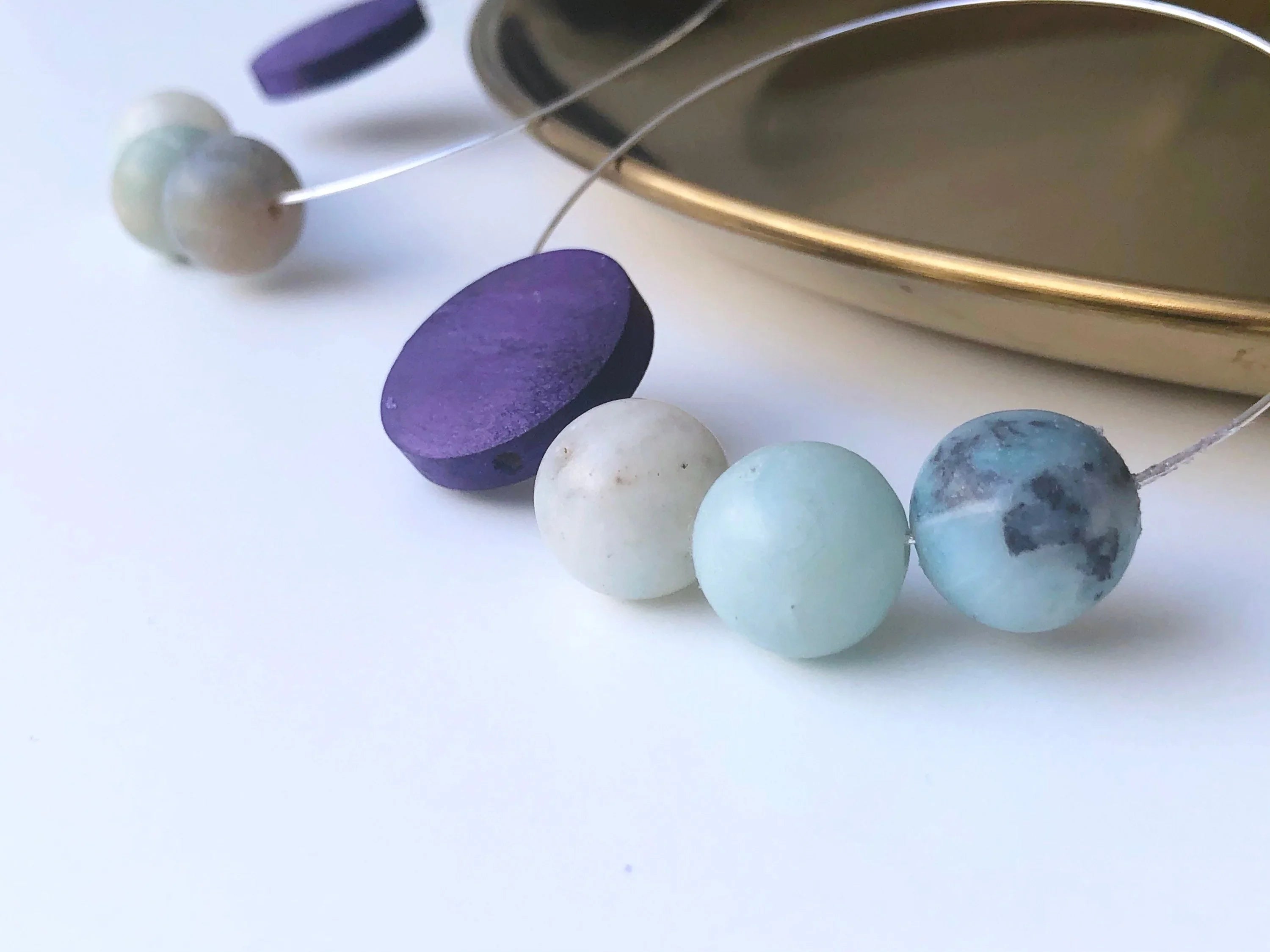 Handmade gemstone necklace with blue, white, and purple beads on a gold tray