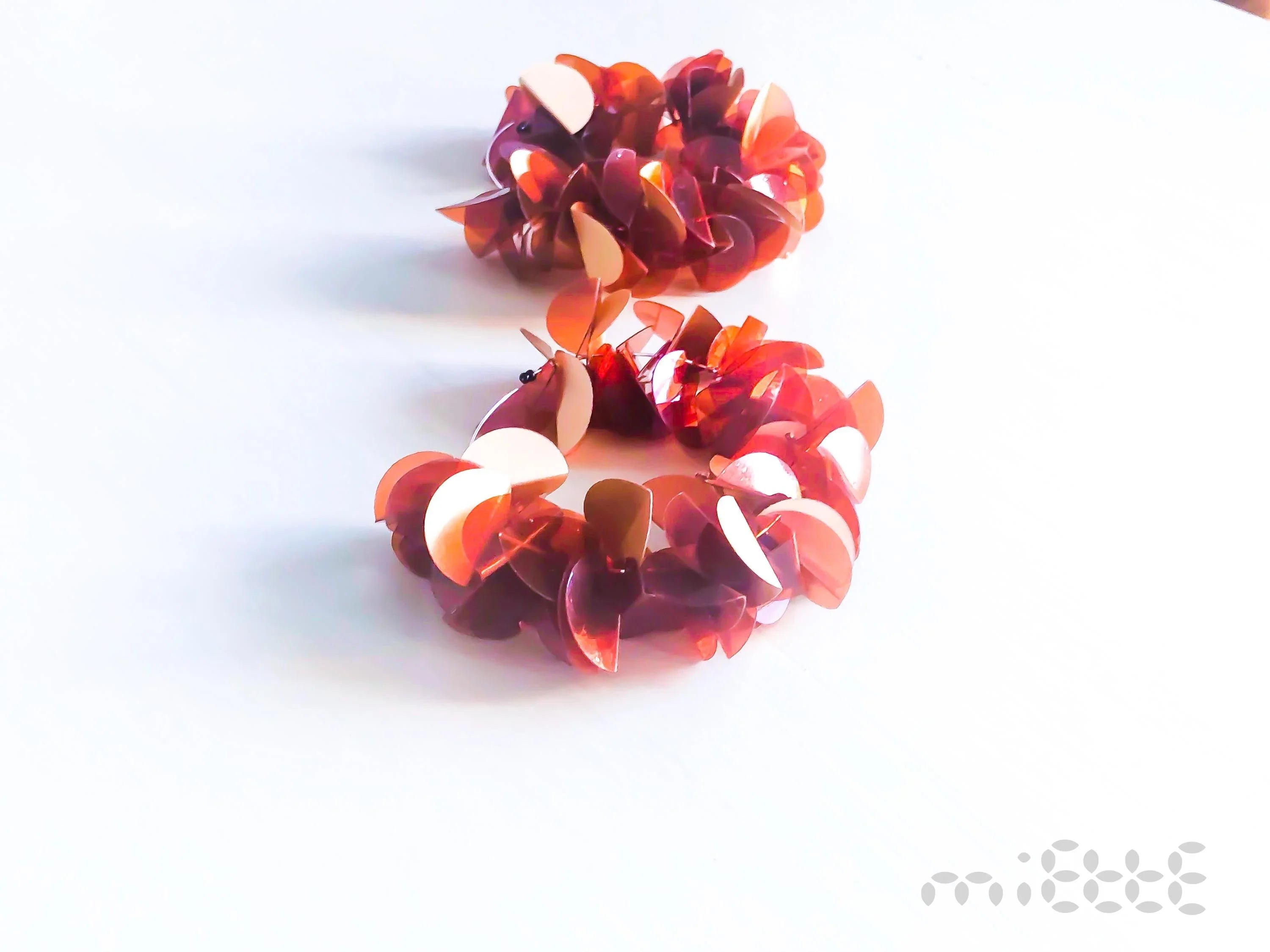 Pair of artisan earrings with red and pink petal shapes on a white background