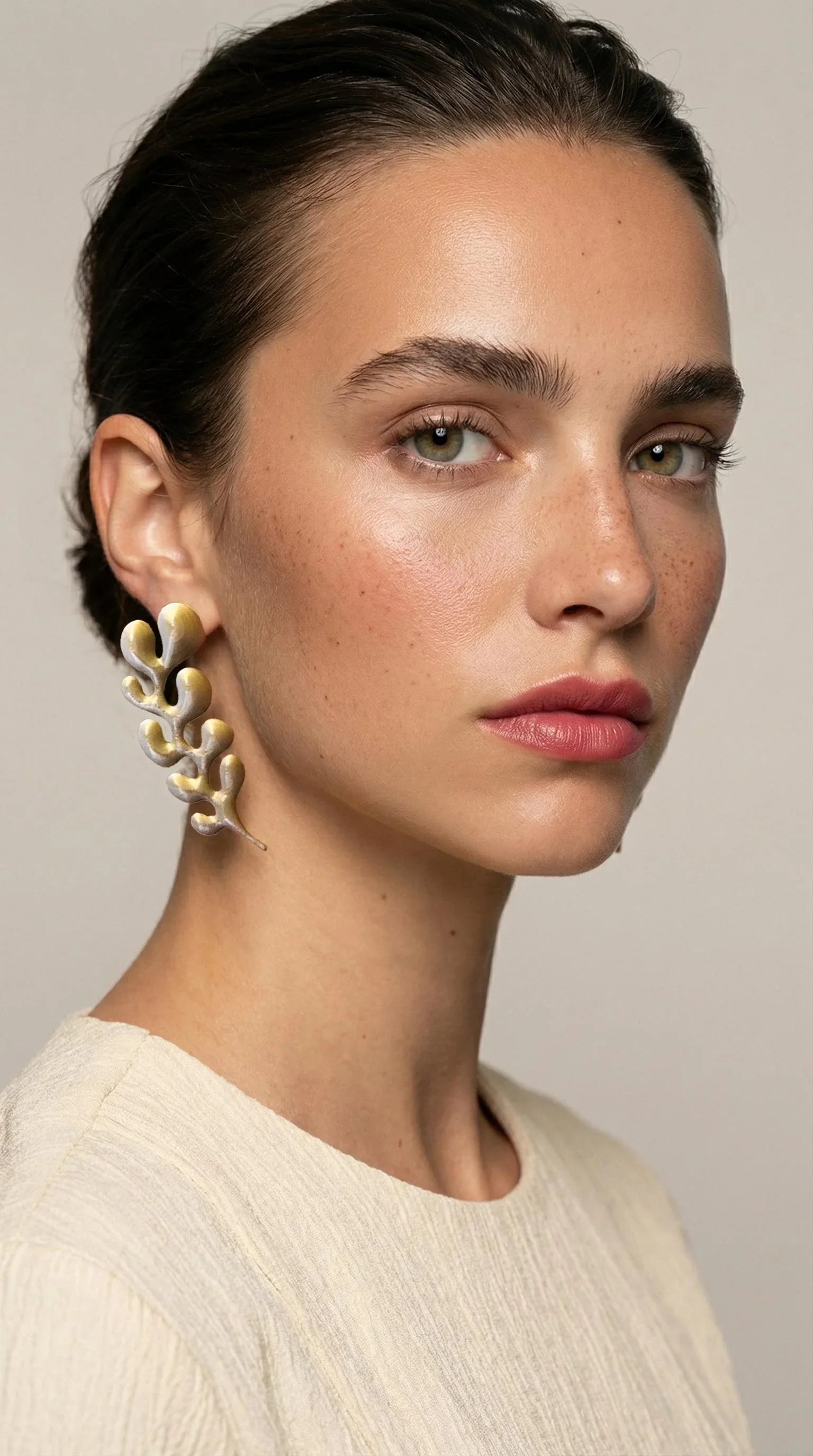Woman wearing sculptural gold statement earring and cream textured top