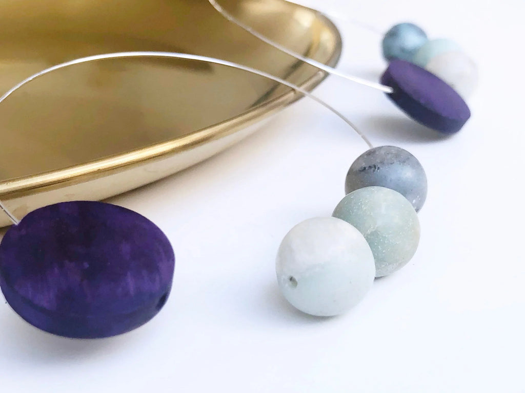 Artisan jewelry with purple and pastel beads on wire, displayed near gold tray