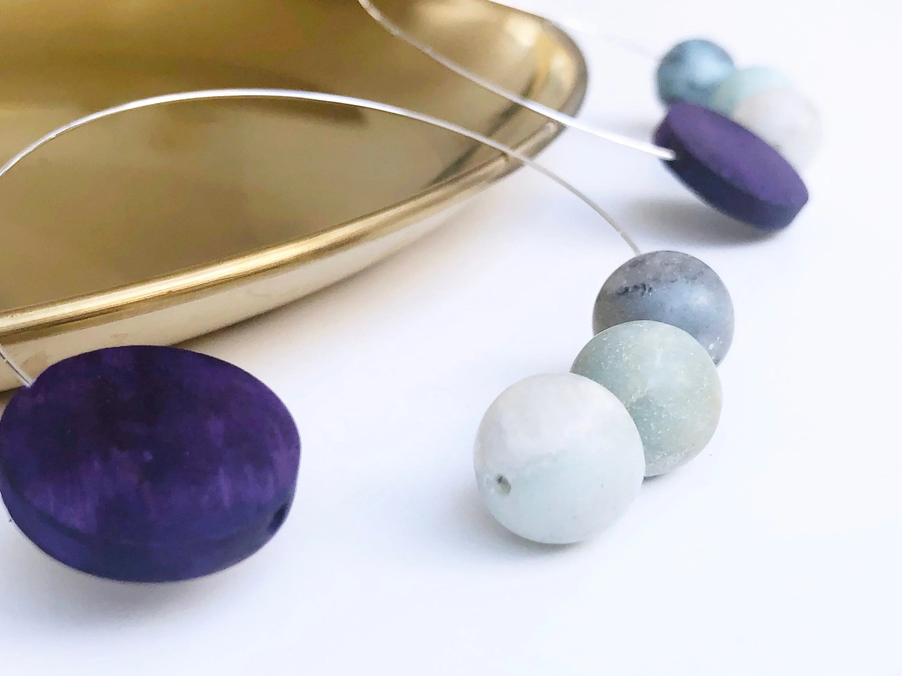 Artisan jewelry with purple and pastel beads on wire, displayed near gold tray