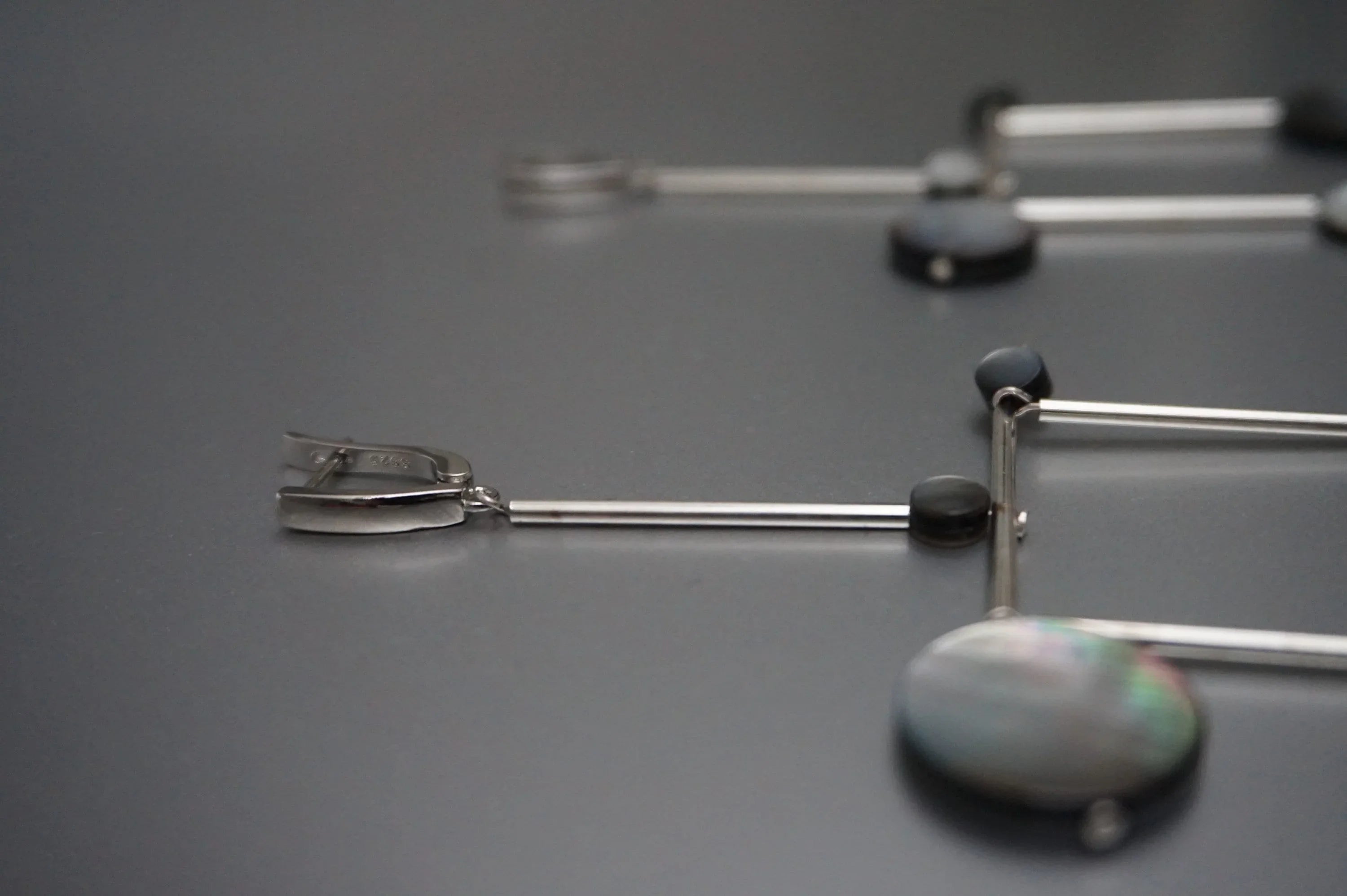 Modern silver and black geometric earrings with round accents on a matte grey surface