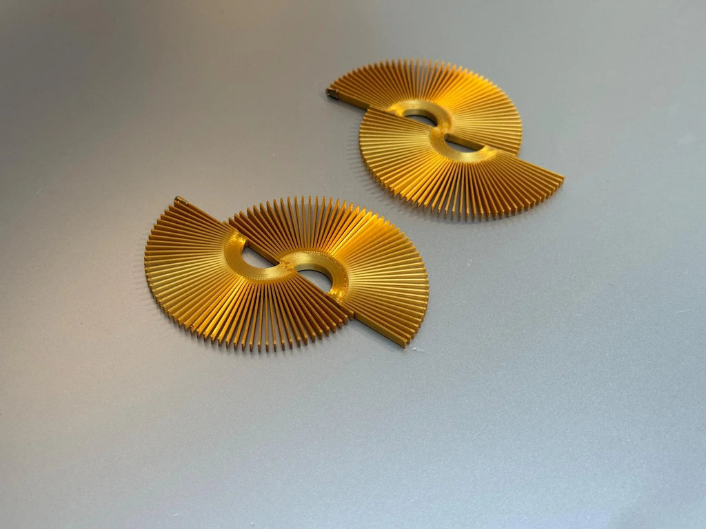 Gold fan-shaped statement earrings with geometric cutout design on a gray background
