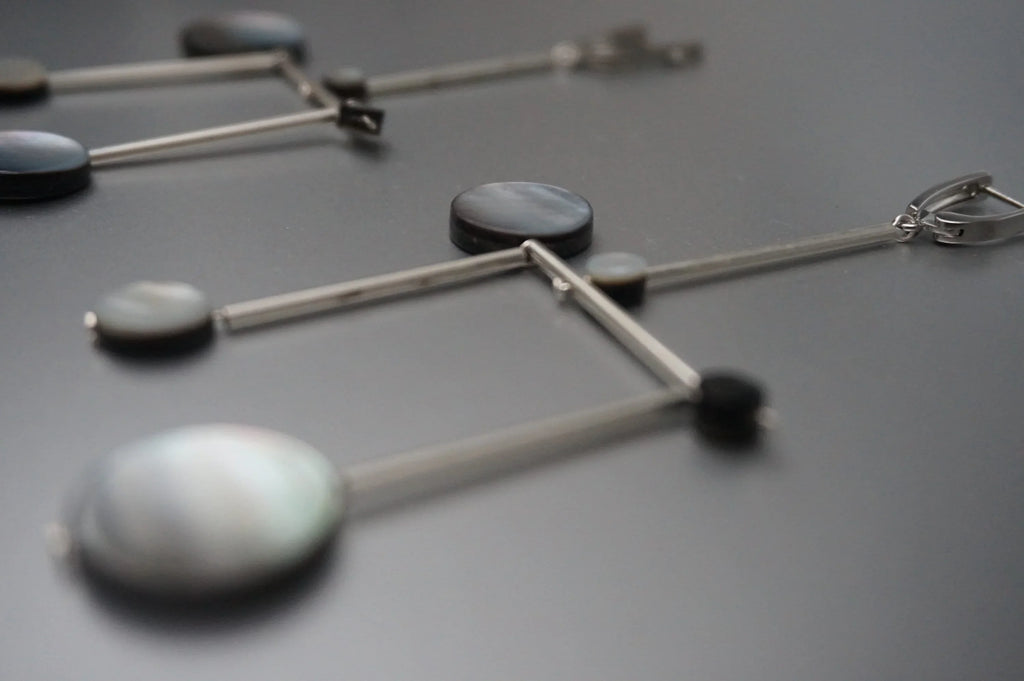 Geometric dangle earrings with silver bars and round shell-like accents on dark surface