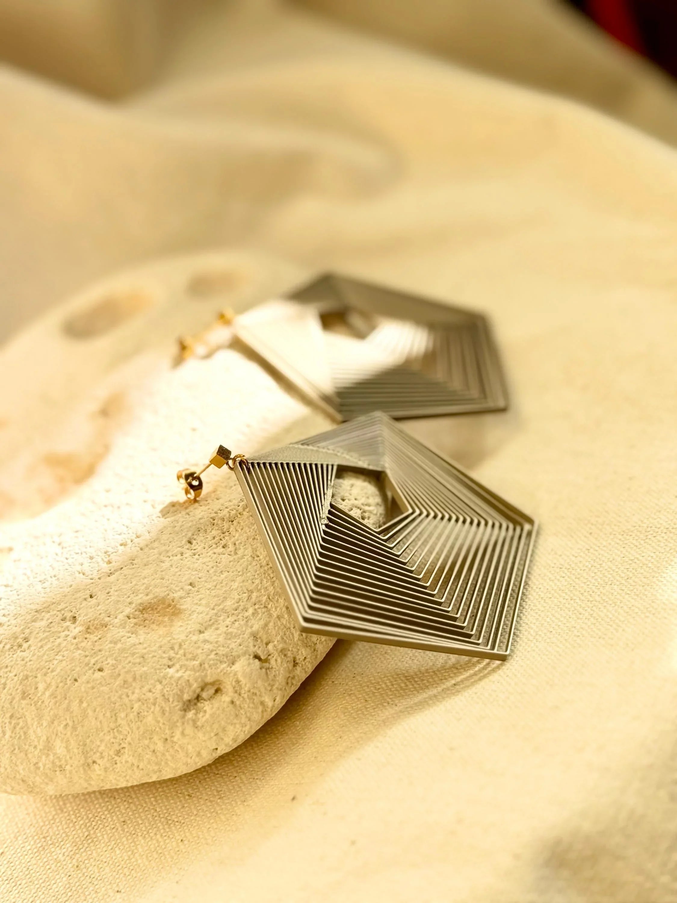Geometric gold earrings with layered pentagon design on a natural stone background