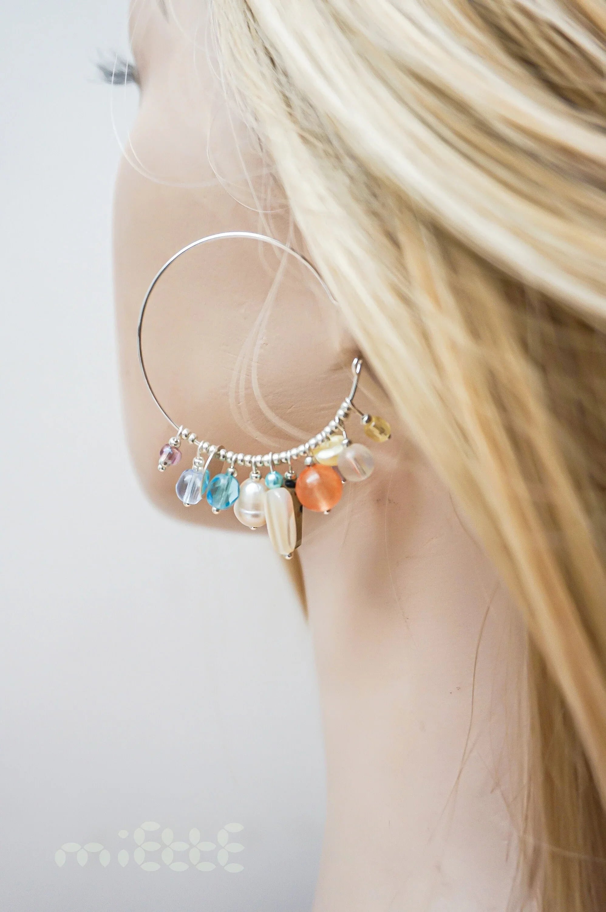 Large silver hoop earring with colorful gemstone and pearl charms on model ear