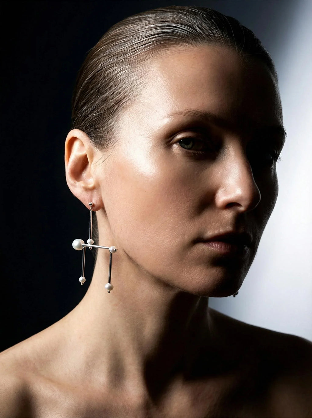 Woman wearing geometric silver and pearl statement earring against dark background