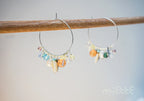 Handcrafted hoop earrings with colorful gemstone beads and pearls on a wooden rod
