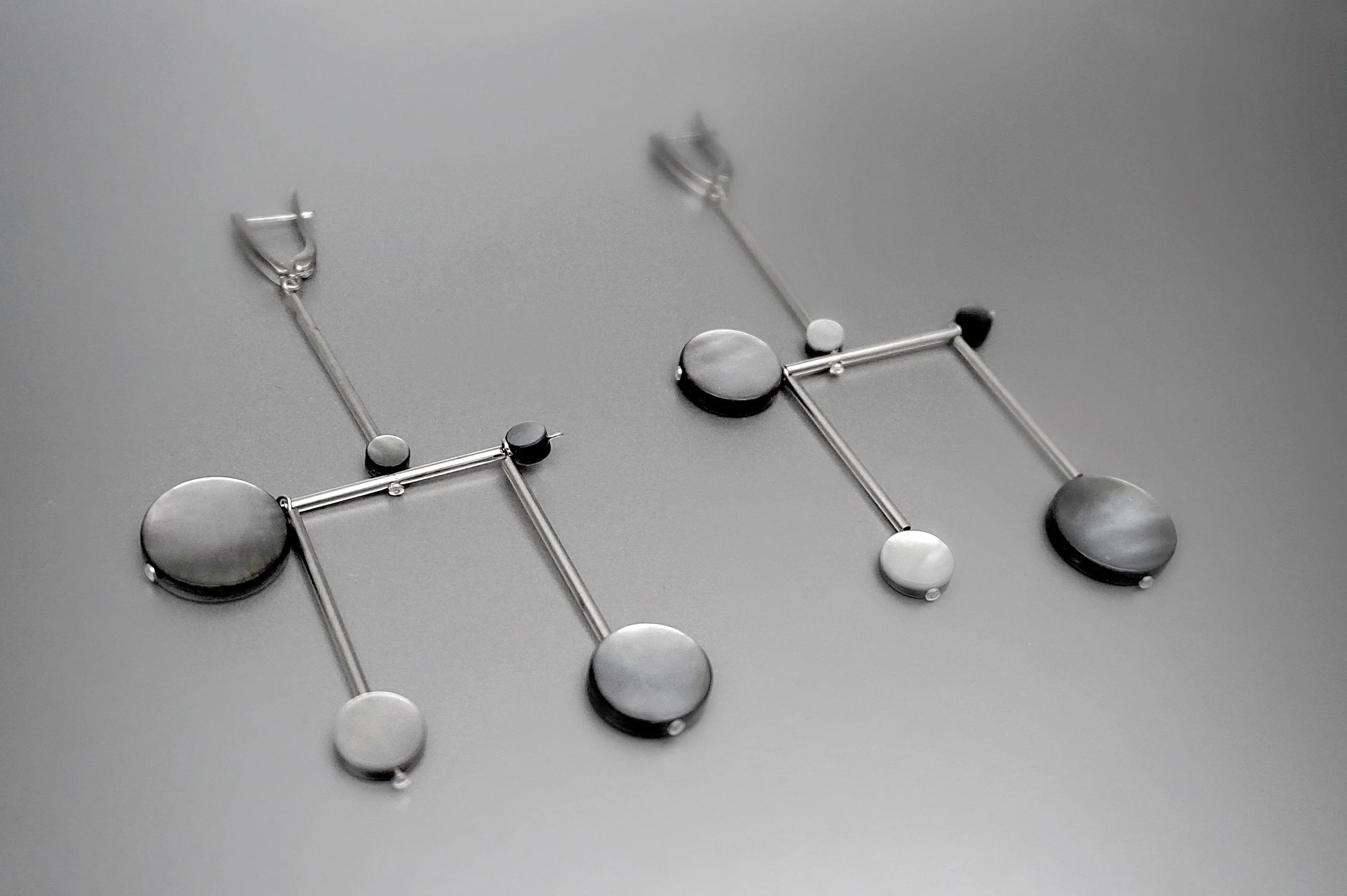 Modern geometric silver earrings with circular and linear elements on gray background