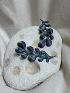Artisan green and purple abstract earrings on a textured stone, minimalist display